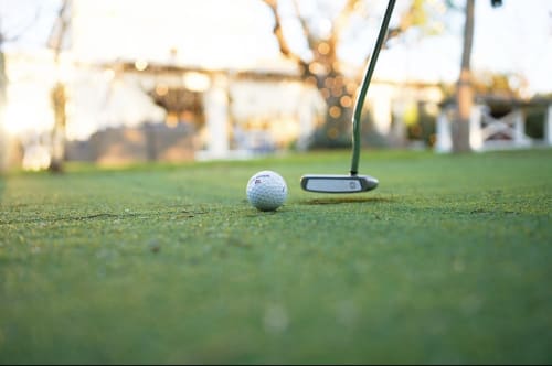 Golf putting green at Masseria Vittoria resort in Acaya, Italy with white ball and putter at sunset