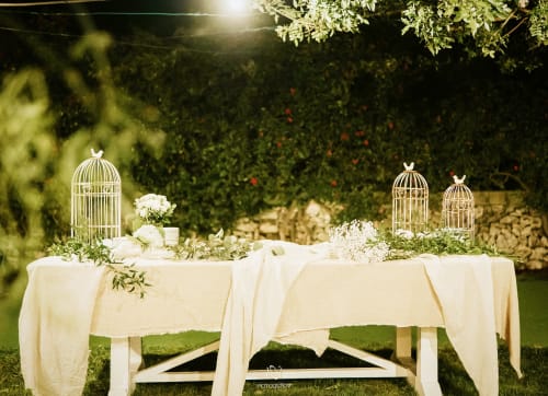 Elegant outdoor garden dinner setup at Masseria Vittoria in Acaya with white birdcages, flowers, and draped tables