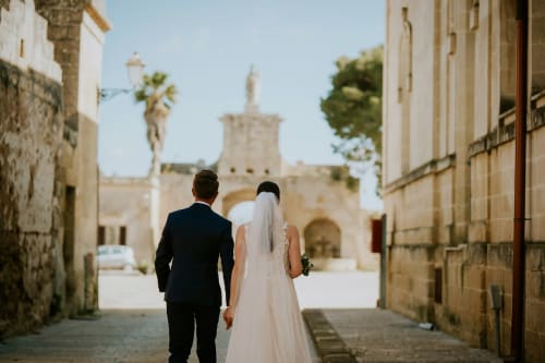 Bride and groom walking toward historic tower in ancient Acaya village, Masseria Vittoria wedding venue