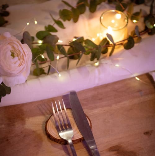 Elegant table setting at Masseria Vittoria with pink ranunculus, string lights, and wooden charger plate in Acaya