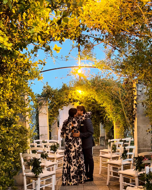 Couple embracing at Masseria Vittoria's evening wedding venue in Acaya, surrounded by golden-lit ivy and white chairs
