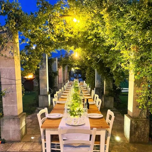 Elegant outdoor dining setup at Masseria Vittoria with long wooden table, white chairs, greenery, and evening lighting in