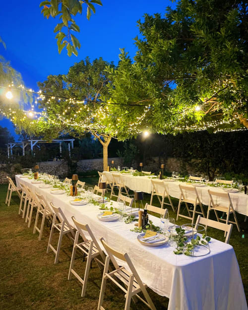 Outdoor evening dinner setup at Masseria Vittoria with string lights, long tables, and lush greenery in Acaya, Italy.