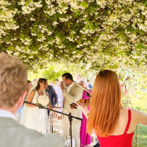 Violinist performing at outdoor wedding venue under blooming white flowers at Masseria Vittoria, Acaya, Italy