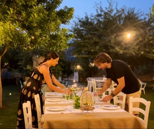 Two guests set elegant outdoor dinner table at dusk in Masseria Vittoria garden, Acaya