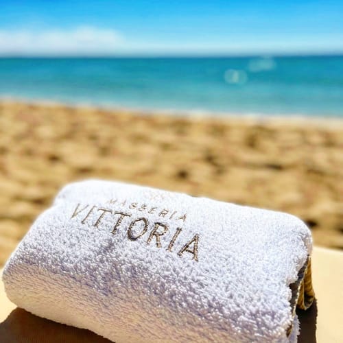 Masseria Vittoria towel on beach with turquoise sea and sandy shore in Acaya, Puglia