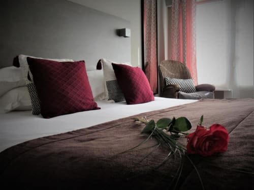 Chambre élégante de l'hôtel Be Hotel Le Touquet avec oreillers bordeaux, une rose rouge sur le lit et vue sur la ville