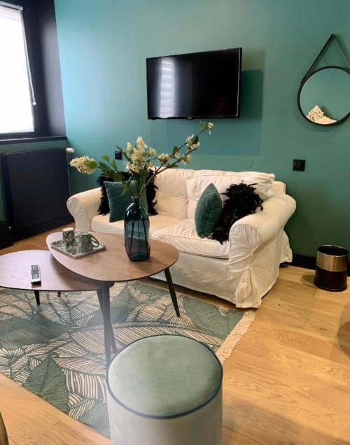Salon moderne turquoise au Be Hotel Le Touquet avec canapé crème, pouf rond, table basse en bois et décor mural