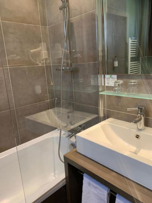 Salle de bains moderne du Be Hotel Le Touquet avec douche en verre, lavabo blanc et carrelage taupe
