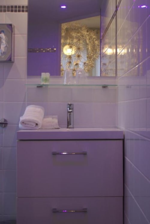 Salle de bains moderne violette avec lavabo, miroir et équipements au Be Hotel Le Touquet