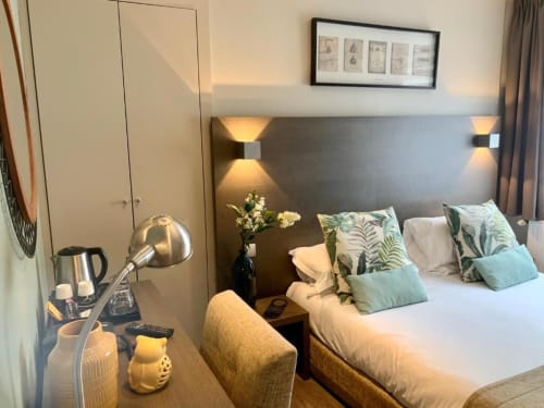 Chambre moderne de l'hôtel Be Hotel Le Touquet avec lit queen-size, oreillers botaniques verts, lampe de bureau et vue sur la ville