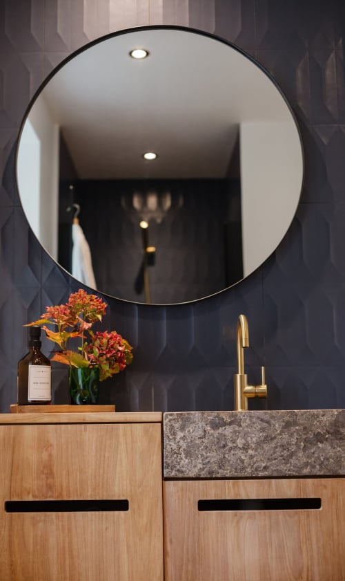 Moderne badkamer bij Moulin Renaudoits met ronde spiegel, houten meubel, koperen kraan en oranje bloemen in Autun