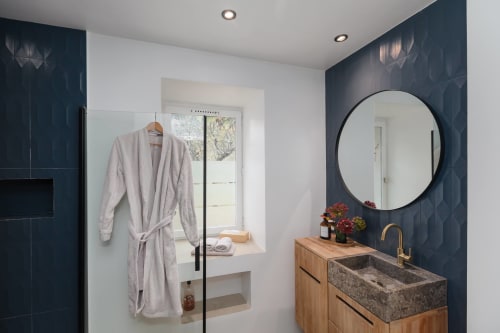 Moderne badkamer in Moulin Renaudiots met donkertealkeurige tegels, houten wastafel, rond spiegelglas en uitzicht op de tuin