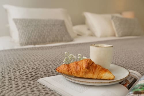 Croissant en koffie op een bordje in appartement Maison Lùisa in Moulin Renaudiots, Autun, met bank en kussens op de achtergrond
