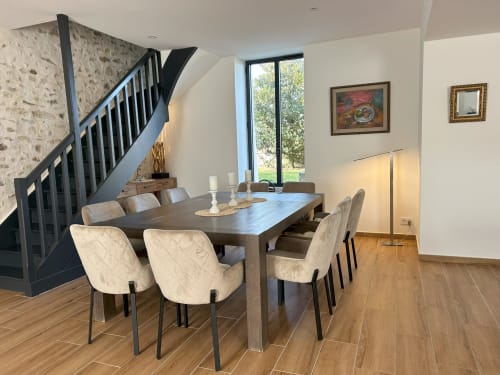 Salle à manger moderne du gîte La Ferme du Châtaignier avec table en bois, chaises rembourrées, escalier et vue sur le jardin