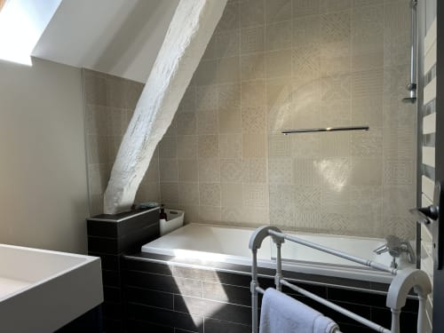 Salle de bain moderne avec carrelage beige à motifs, baignoire noire, cabine de douche vitrée et plafond mansardé à La Ferme du