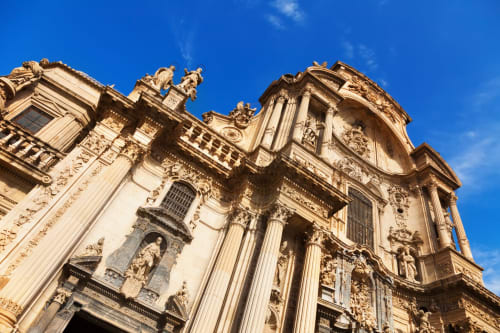 Ornamentada fachada de catedral barroca con columnas de piedra dorada y esculturas bajo cielo azul, León España