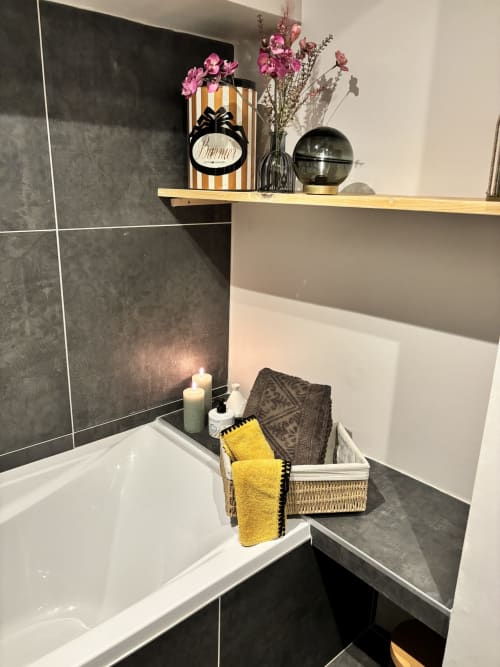 Salle de bain élégante au gîte La vie de château à Grignan avec carrelage noir, baignoire blanche, serviettes jaunes, fleurs roses et bois