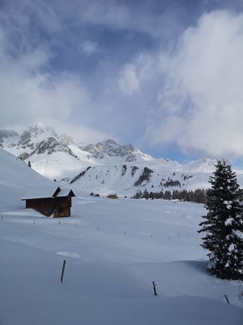Paesaggio alpino innevato con casetta da barca in legno, montagne e alberi sempreverdi vicino a Treviso