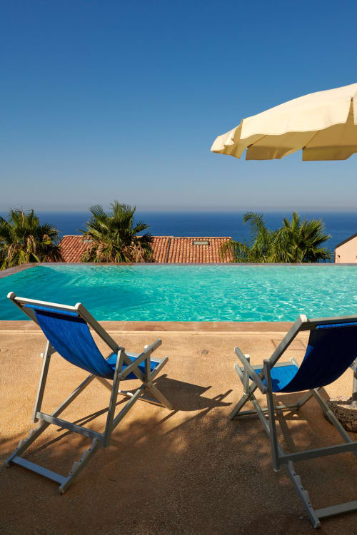 Beachfront pool with blue loungers, palm trees, and Mediterranean sea view at CefalHome hotel, Italy