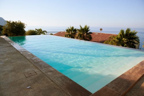 Infinity pool with turquoise water overlooking sea, palm trees, and terracotta roof at CefalHome Roma