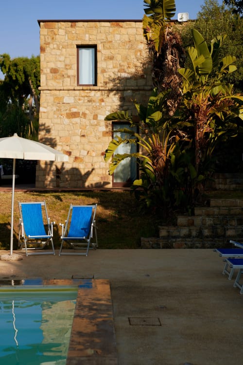 CefalHome pool area with stone villa, blue loungers, and tropical plants in Rome