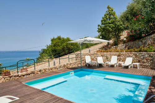 CefalHome luxury pool terrace with turquoise water, white lounge chairs, umbrella, and Mediterranean sea view from Roma