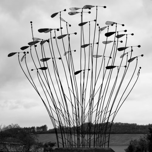 Modern metal sculpture resembling grass with paddle elements overlooking water at Domaine de l'Ocrerie in Pourrain