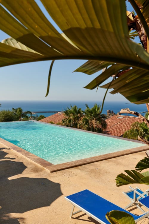 Piscina turchese con vista sul mare, palme e ombrelloni gialli nella proprietà CefalHome a Roma