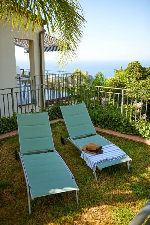 Turquoise lounge chairs on a lawn overlooking the Mediterranean Sea at CefalHome hotel in Rome
