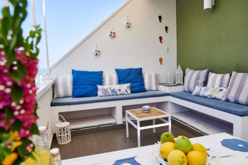 CefalHome's rooftop terrace in Rome with blue cushioned seating, striped pillows, sea views, and fresh lemons on a table