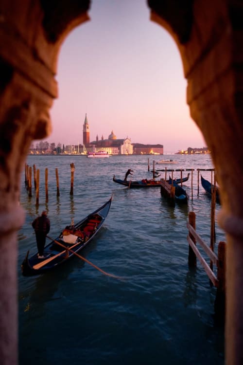 Gondole veneziane al tramonto incorniciate da un arco in pietra, con la basilica di San Giorgio Maggiore sullo sfondo vicino a Treviso