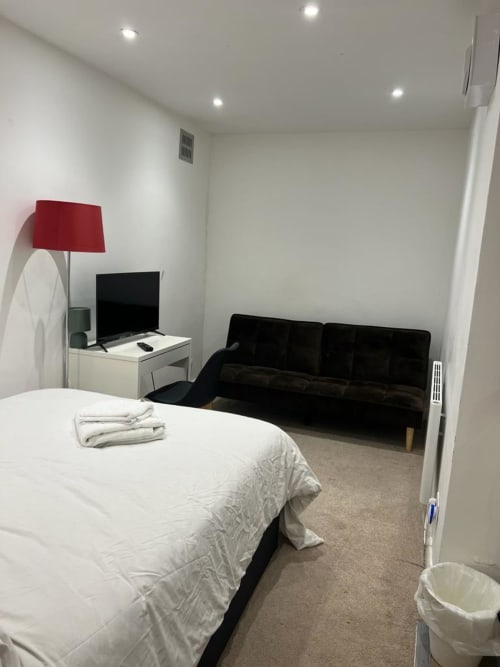 Modern bedroom with white bed, black sofa bed, desk with red lamp and TV at Starlet Property London