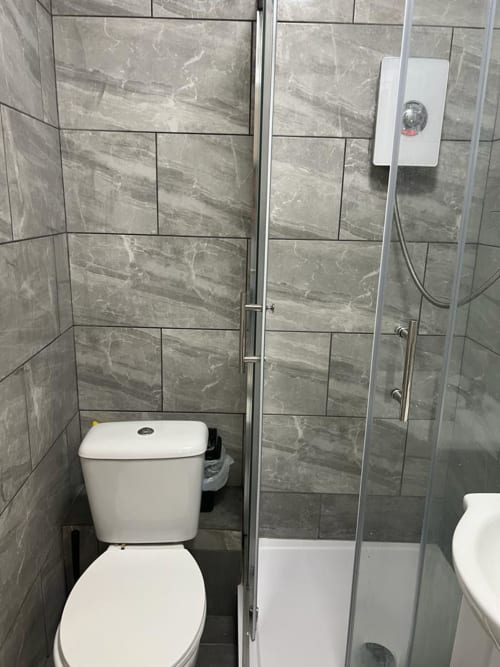 Modern bathroom at Starlet Property London with gray marble tiles, white toilet, shower enclosure and wall-mounted heater