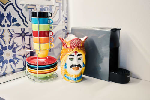 Colorful kitchen décor at CefalHome Roma: stacked mugs on stand, decorative Sicilian head vase, and coffee maker