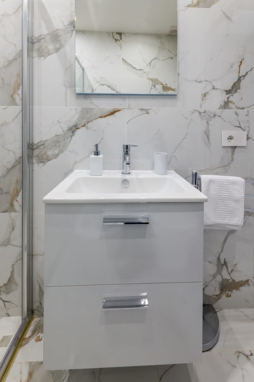 Bagno moderno in marmo presso hotel di Napoli con lavabo bianco, rubinetteria cromata e porta asciugamani decorativo