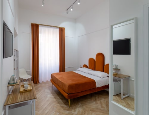 Modern Standard Room at Garibaldi 125 Naples with orange bed, flat-screen TV, work desk, and city views through curtained