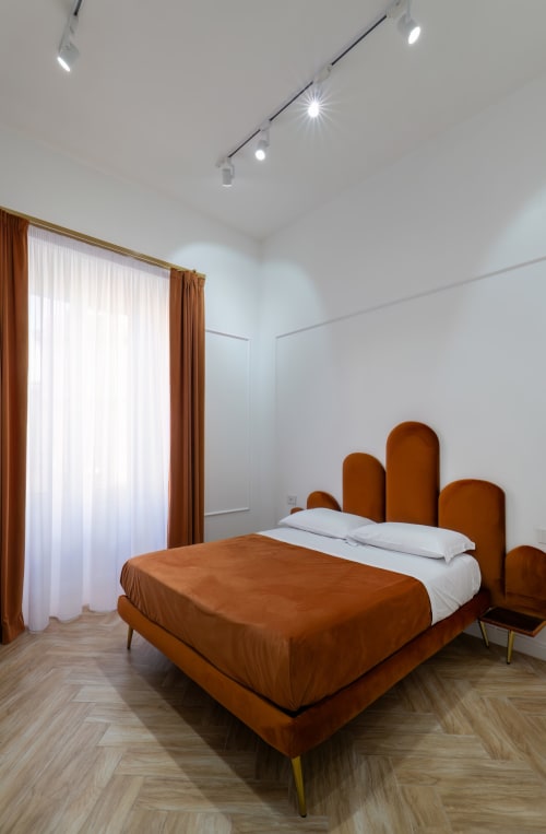 Modern bedroom at Garibaldi 125 Naples with burnt orange upholstered bed, white pillows, wooden herringbone flooring, and