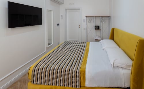 Modern double room at Garibaldi 125 Naples with yellow upholstered bed, flat-screen TV, and contemporary décor