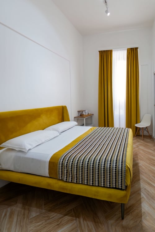 Bright double bedroom at Garibaldi 125 in Naples with mustard velvet bed, white linens, and matching curtains