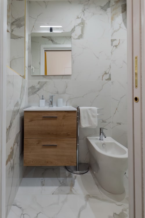 Modern bathroom with marble walls, wooden vanity, mirror, and bidet at Garibaldi 125 Naples hotel room