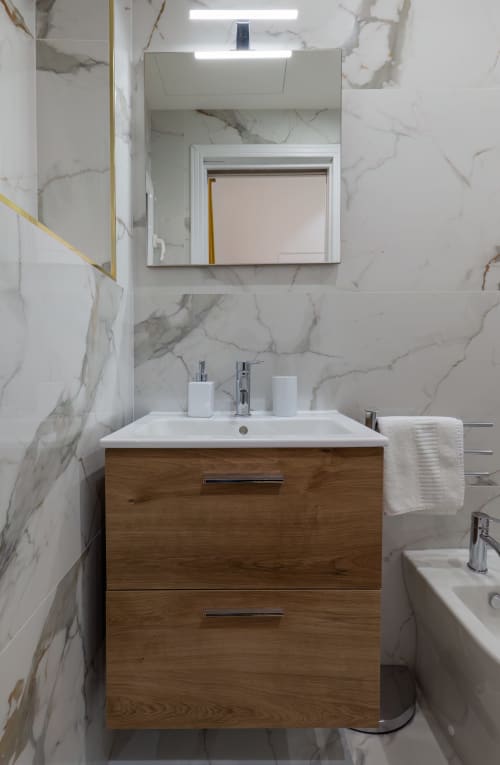 Modern bathroom with marble walls, wooden vanity, white sink, and illuminated mirror at Garibaldi 125 in Naples