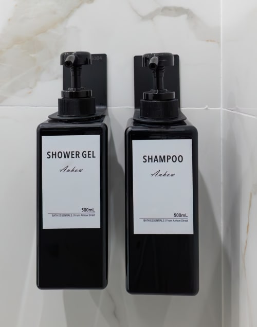 Two black Anhow bath amenity bottles with shower gel and shampoo on marble bathroom wall at Garibaldi 125 in Naples