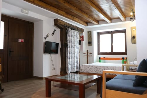 Espaciosa habitación del hotel Casa Lafuente en Lukiano con vigas de madera vista, cama, TV y vistas a la montaña desde grandes ventanas