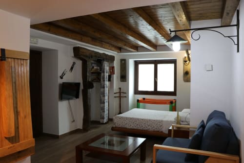 Acogedora habitación en Casa Lafuente, Lukiano, con vigas de madera vista, cama, TV y vistas a las montañas.