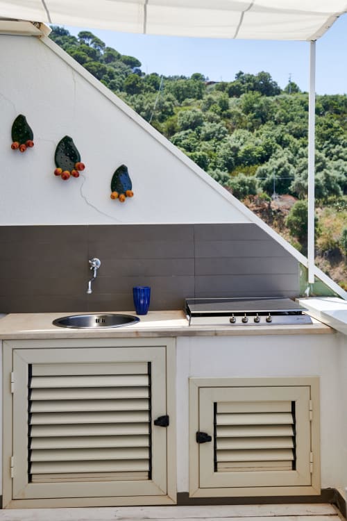 Modern outdoor kitchen at CefalHome with sink, cooktop, and decorative wall art overlooking lush hills in Rome