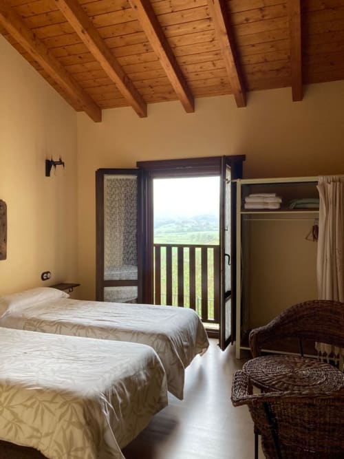 Habitación luminosa con dos camas individuales, vigas de madera vista, balcón con vistas a las montañas en Casa Lafuente, Araba