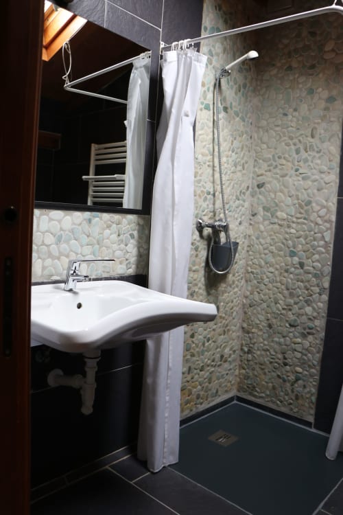 Baño moderno con azulejos texturizados en piedra, lavamanos pedestal, espejo y ducha tipo walk-in en Apartamentos Casa Lafuente