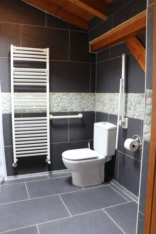 Baño moderno en Casa Lafuente con paredes de azulejos oscuros, inodoro blanco, toallero térmico y azulejos de piedra decorativos en Lukiano,