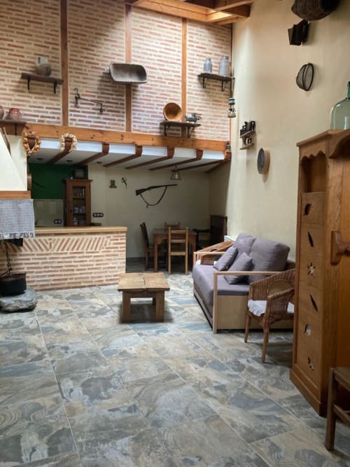 Rústica sala de estar con paredes de ladrillo, vigas de madera, suelos de piedra y vistas a la montaña en Casa Lafuente, Lukiano